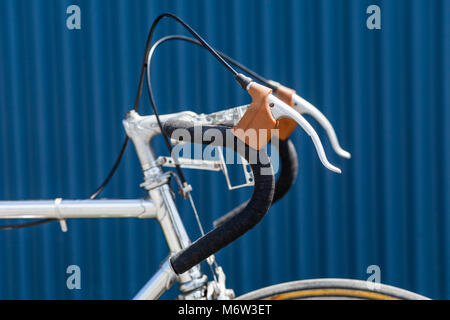 Handlbars avec du ruban adhésif noir et leviers de frein de vieux vélos de course avec cadre chrome en avant du mur bleu Banque D'Images