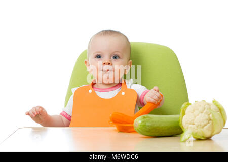 Avoir un bébé table pleine de légumes sains. Cheerful toddler mangeant des carottes. Isolé sur fond blanc. Banque D'Images