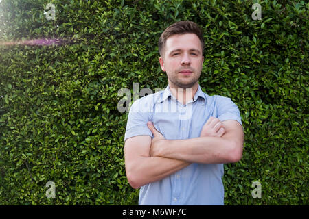 Man in blue shirt debout près de la paroi de l'herbe verte. Il est souriant et très confiant. Banque D'Images