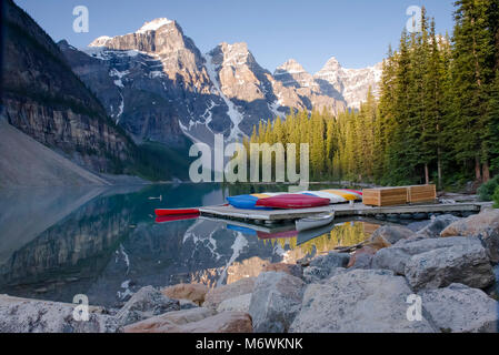 Canots aux couleurs vives sur une jetée, lac Moraine, Alberta, Canada. La lumière du matin illumine les sommets enneigés