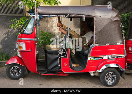 Vue horizontale d'un conducteur de pousse-pousse endormi à l'arrière de son véhicule à Colombo, Sri Lanka. Banque D'Images