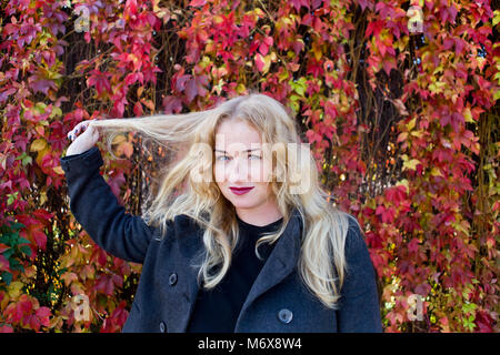 La femme blonde joue avec ses cheveux et se tenant dans le parc coloré Banque D'Images