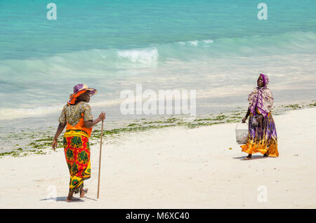 Zanzibar, Tanzanie - le 4 décembre 2014 : Les femmes avec des vêtements colorés à marcher le long de la plage de Nungwi. Banque D'Images