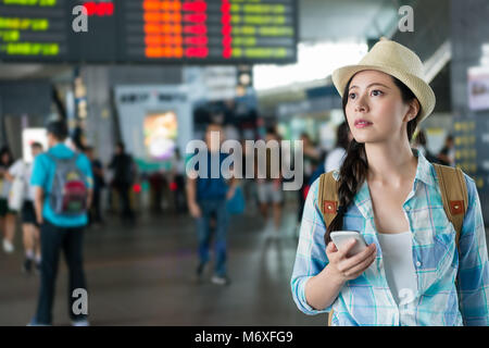 Jeune femme voyage sortie du hall de la station debout à la plate-forme et la tenue d'un smartphone à la direction pour le prochain voyage. Banque D'Images