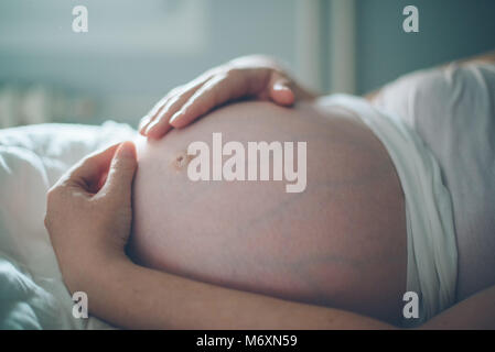 Femme enceinte ventre câlins dans la chambre à la maison juste avant le travail et l'accouchement, selective focus Banque D'Images