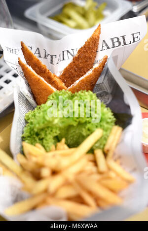 Crumbed des portions de poisson frit servi avec frites et salade verte à froufrous frais sur journal dans un restaurant ou des pêches Banque D'Images