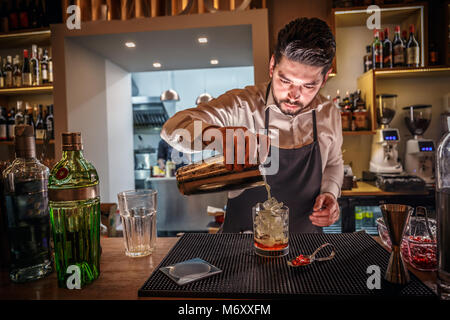 Homme barman est de faire couler l'alcool à partir de cocktail shaker à fond de verre au bar Banque D'Images