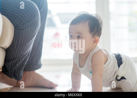 Neuf mois bébé garçon ramper vers le père. La famille asiatique à la maison, vivant à l'intérieur de style de vie. Banque D'Images