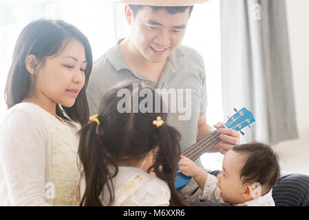 Les parents et les enfants chanter et jouer ukulele ensemble. La famille asiatique passer du temps de qualité à la maison, vivant à l'intérieur de style de vie. Banque D'Images