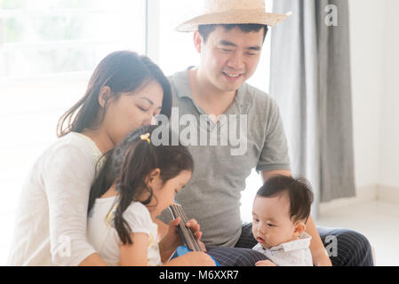 Les parents et les enfants chanter et jouer ukulele ensemble. La famille asiatique passer du temps de qualité à la maison, vivant à l'intérieur de style de vie. Banque D'Images