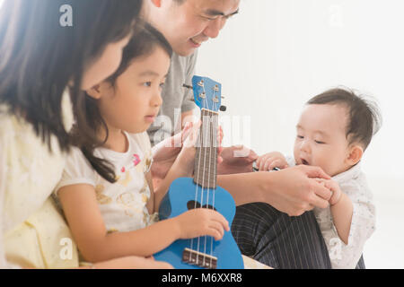 Les parents et les enfants à l'ukulele ensemble. La famille asiatique passer du temps de qualité à la maison, mode de vie naturel à l'intérieur. Banque D'Images