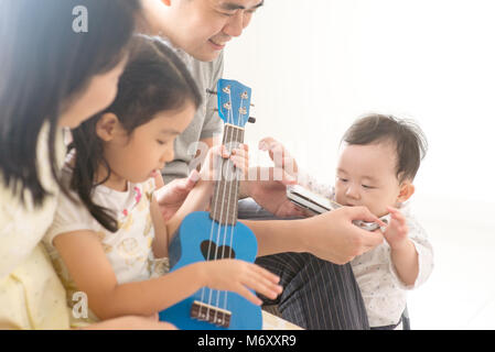 Les parents et les enfants chantant et jouant de l'harmonica ukulele et ensemble. La famille asiatique passer du temps de qualité à la maison, mode de vie naturel à l'intérieur. Banque D'Images