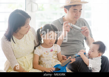 Les parents et les enfants chantant et jouant de l'harmonica ukulele et ensemble. La famille asiatique passer du temps de qualité à la maison, vivant à l'intérieur de style de vie. Banque D'Images