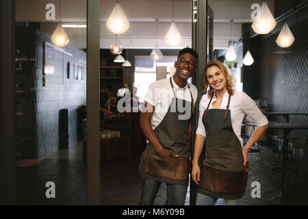 Heureux propriétaire d'une boutique de café couple standing dans leur boutique. L'homme et la femme des baristas debout à leur café portant un tablier. Banque D'Images