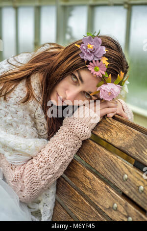 Femme portant une coiffe de fleurs s'appuyant sur un banc en bois Banque D'Images