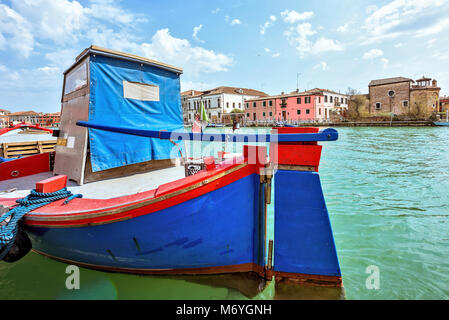 Vue de l'heure bleue et rouge coloré dynamique voile stationné dans la lagune vénitienne. Bâtiments lumineux et ciel bleu avec des nuages sur l'arrière-plan. L'île de Murano, Banque D'Images