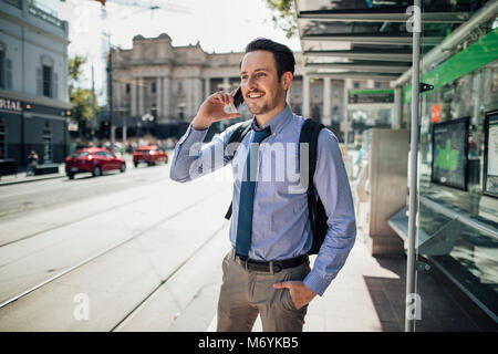 Businessman millénaire parle sur son smartphone en attendant un tram à Melbourne, Victoria. Banque D'Images