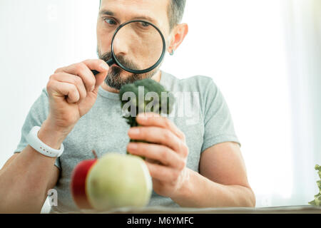 Recherche curieux homme tenant un brocoli à la loupe à travers. Banque D'Images