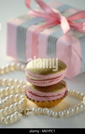 L'or et rose macarons chocolats français, avec une tasse de thé, de perles et d'une élégante boîte cadeau rose. Cadeaux de luxe. Banque D'Images