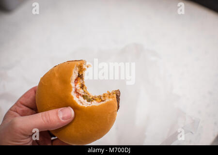 Burger fromage unique avec une morsure pris hors de lui. Preuve de la graisse wrapper papier en arrière-plan Banque D'Images