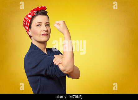 Sûr de femme d'âge moyen avec un poing serré retrousser sa manche, l'espace texte, hommage à l'icône américaine à riveter Rosie Banque D'Images