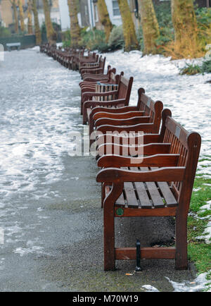 Rangée de bancs en bois dans un parc avec de la neige mouillée sur le terrain - focus sélectif. Banque D'Images