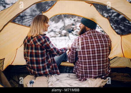 Jeune couple s'assied et sourit en jaune tente tourisme randonnée en hiver. Vue arrière. Banque D'Images