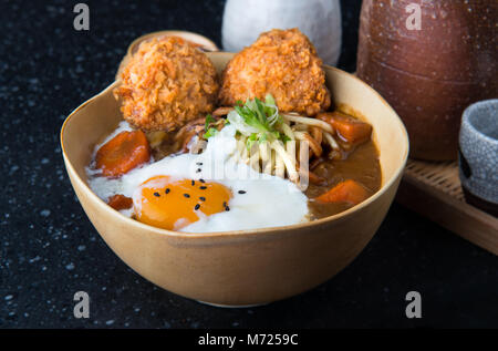 Curry japonais avec des nouilles Udon et croustillant côtelette croquettes et oeuf dur topping sur bol tasse style. Banque D'Images