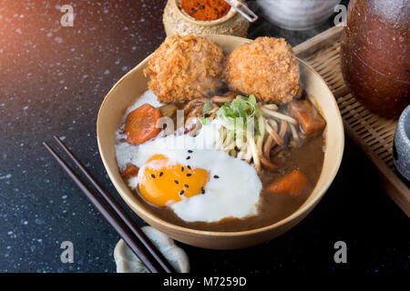 Curry japonais avec des nouilles Udon et croustillant côtelette croquettes et oeuf dur topping sur bol tasse style. Banque D'Images