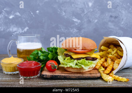 Burger Juteux, frites, sauces, de la bière sur un fond de bois. Le fast food. L'alimentation de rue. Banque D'Images