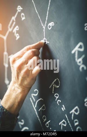 L'enseignant écrit sur un tableau à la craie une formule pour le courant électrique. Banque D'Images