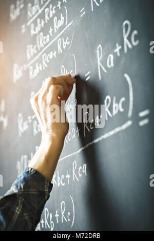 L'enseignant écrit sur un tableau à la craie une formule pour le courant électrique. Banque D'Images