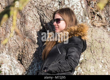 Pretty young woman posing par un arbre à l'extérieur en hiver avoir sa photo prise. Banque D'Images