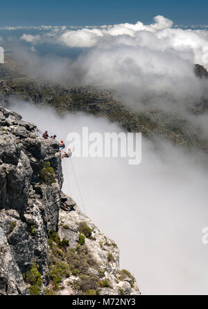 Abseilers la descente en rappel sur le sommet de la Table Mountain à Cape Town avec le nuage-enveloppé Douze Apôtres montagnes en arrière-plan. Banque D'Images