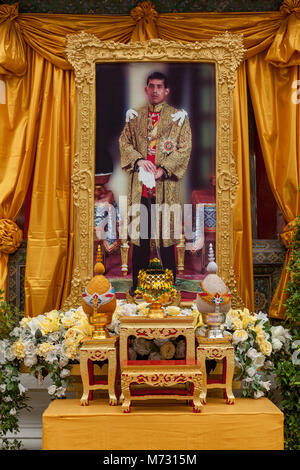 Photo encadrée de Thai actuel roi Maha Vajiralongkorn Bodindradebayavarangkun Rama X, derrière un autel avec des fleurs, entouré de rideaux orange Banque D'Images