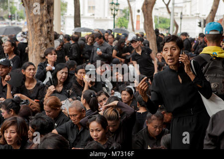 Foule de gens sur le trottoir en Ratchadamnoen Road à Bangkok le jour de la Crémation Royale, assis en attente dans leurs vêtements noirs Banque D'Images