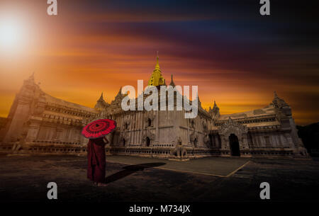 Asian young monk holding parapluie rouge sur l'Ananda temple au coucher du soleil à Bagan, Myanmar. Banque D'Images