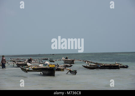 Les bateaux de pêche traditionnels Dhow à Jambiani Zanzibar Tanzanie port à marée basse avec un pêcheur en poussant le bateau sur la mer Banque D'Images