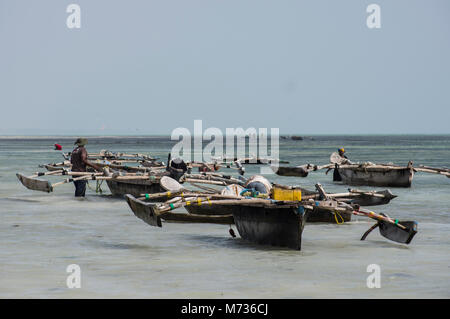 Les bateaux de pêche traditionnels Dhow à Jambiani Zanzibar Tanzanie port à marée basse avec un pêcheur en poussant le bateau sur la mer Banque D'Images