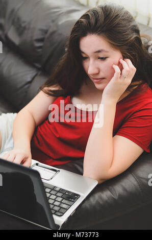 Femme assise confortablement sur le canapé à la maison à l'aide d'un ordinateur portable. Femme jouant de concentré, la lecture, regarder à l'écran de l'ordinateur portable. Banque D'Images