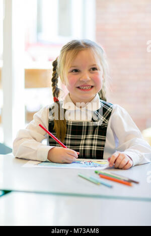 Écolière primaire assis à une petite table à dessin, up smiling avec un crayon à la main Banque D'Images