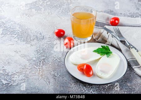 Deux œufs au plat pour le petit-déjeuner sain sur une plaque blanche avec des tomates cerises et verre de thé Banque D'Images