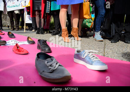 08 mars 2018, l'Allemagne, Stuttgart : Les femmes debout par un tapis, qui est couverte d'affiches. Le Conseil d'État sont des femmes à l'aide de cette campagne de lutte pour l'égalité entre les hommes et les femmes : Un tapis rose avec une rangée de paires de chaussures chaussures unique composé de des hommes et des femmes. Photo : Sina Schuldt/dpa Banque D'Images