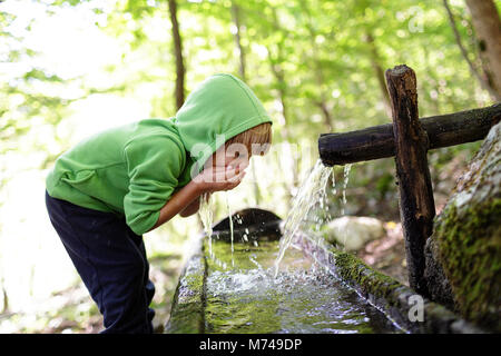 Jeune garçon blond l'eau potable de creux des mains de l'auge rustique dans une forêt Banque D'Images