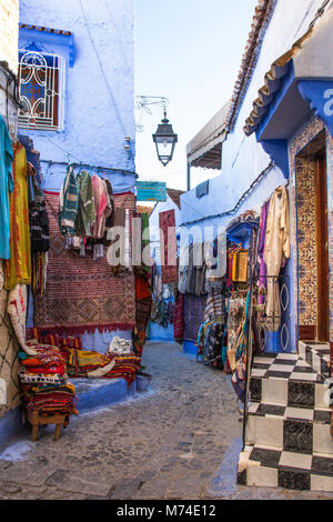 Tapis Tapis Tapis et vêtements de style traditionnel en vente sur l'affichage en scène de rue pavées étroites colorées dans la ville bleue de Chefchaouen, Maroc. Banque D'Images