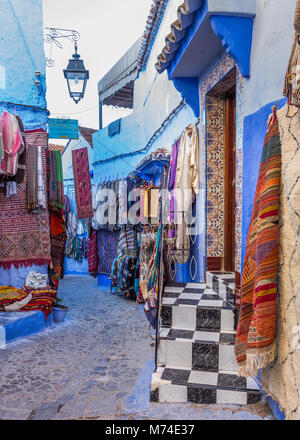 Tapis Tapis Tapis et vêtements de style traditionnel en vente sur l'affichage en scène de rue pavées étroites colorées dans la ville bleue de Chefchaouen, Maroc. Banque D'Images