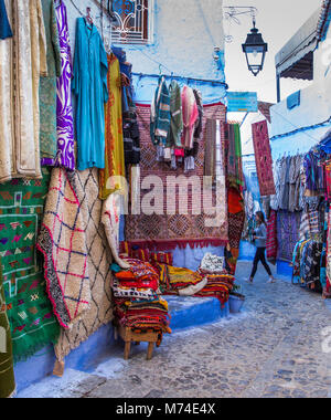 Tapis Tapis Tapis et vêtements de style traditionnel en vente sur l'affichage en scène de rue pavées étroites colorées dans la ville bleue de Chefchaouen, Maroc. Banque D'Images