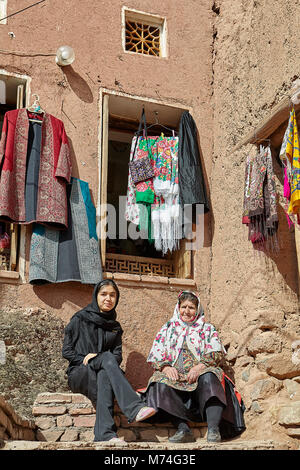 Abyaneh, Iran - le 26 avril 2017 : deux femmes iraniennes sont assis dans un village traditionnel dans les montagnes derrière eux, accrocher les vêtements sur des cintres. Banque D'Images