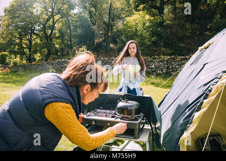 Femme mature essaie de mettre la cuisinière à gaz pour faire elle-même et sa petite-fille une tasse de thé. Banque D'Images