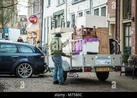 KAMPEN, Pays-Bas - 30 NOVEMBRE 2017 : Un homme est l'emballage des meubles sur une petite remorque derrière une voiture dans une rue de Kampen. Banque D'Images